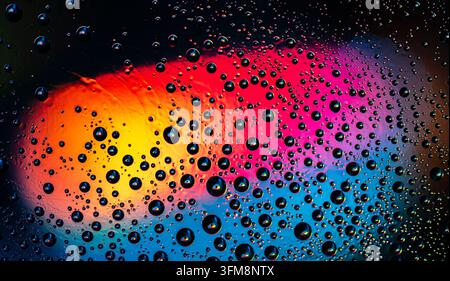 Water drops creating a dynamic abstract pattern, reflecting and refracting a vivid rainbow gradient with soft bokeh Stock Photo