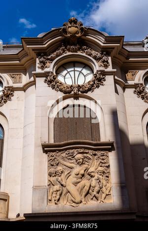 Ornate historical building facade featuring a classic stone bas-relief and an architectural round window under a sunny blue sky scene Stock Photo