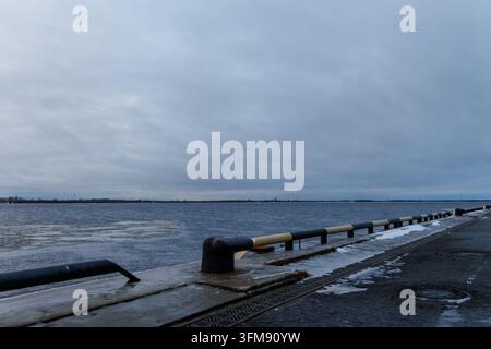 Industrial waterfront terminal with freezing water and ice under dramatic cloudy sky in northern port. Stock Photo