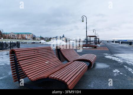 Contemporary street furniture and curved park benches on a deserted city embankment under overcast subarctic sky. Stock Photo
