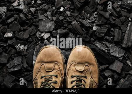 Hard work and industrial labor, pair of worn leather work boots standing on a pile of black coal for construction and mining industry background Stock Photo
