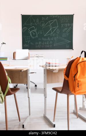 Education and remote learning, empty classroom with math formulas on chalkboard and student desks with laptop and backpack for school or university Stock Photo