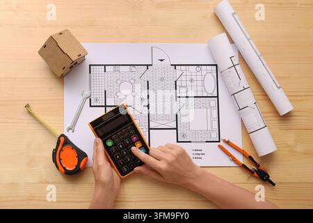 Home renovation budget and construction planning, person using calculator on architectural floor plan with blueprints and measuring tools on wooden de Stock Photo