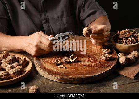 Healthy nutrition and mindful eating, person cracking walnuts with a metal nutcracker on a rustic wooden board for organic food preparation at home Stock Photo