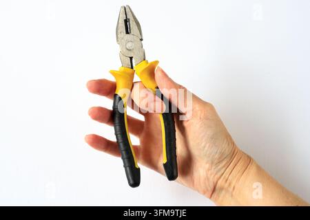 Insulated pliers held in hand for electrical installation and safety work. Electrician service concept for secure wire gripping and technical repair. Stock Photo