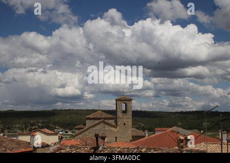 View over traditional terracotta tile roofs towards an old stone church bell tower under a dramatic cloudy blue sky in a Spanish village. Stock Photo