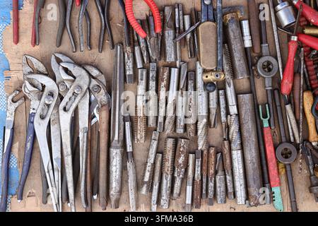 Secondhand metalworking tools for sale, adjustable pliers, brass die stock, threaded metal rods, worn wooden surface, overhead view. Stock Photo