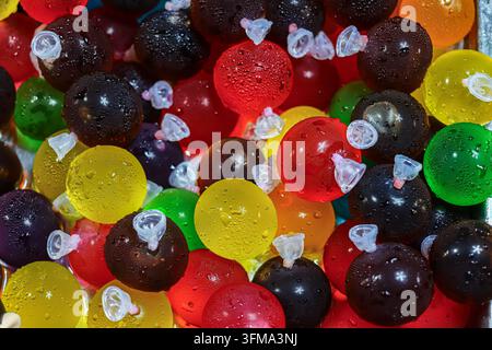 Colorful fruit jelly balls with water droplets piled in a chilled metal tray at a Thai market stall, round sweets in clear plastic balloon packs Stock Photo