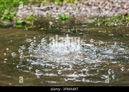 Rainwater splashing into a shallow puddle on concrete ground with floating bubbles, close up, daytime rain in tropical Thailand Stock Photo