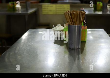 Empty stainless steel dining table with stainless chopstick holder, condiment set and covered ceramic container at a Thai restaurant. Stock Photo