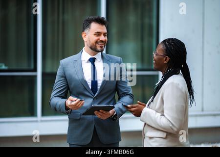 Two diverse business professionals engaging in a discussion and smiling, holding digital devices Stock Photo