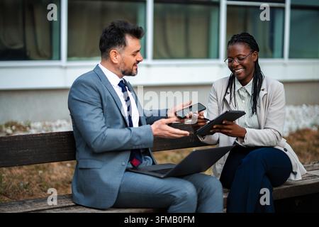 Business colleagues collaborating outdoors using digital tablet and smartphone Stock Photo