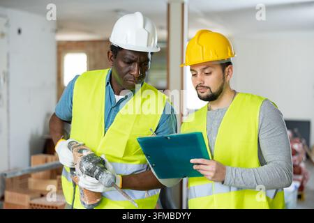 African-american and caucasian men engineers having conversation about project documentation in construction site. Stock Photo