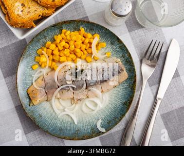 Sliced pickled herring fillet with corn and onions on plate Stock Photo