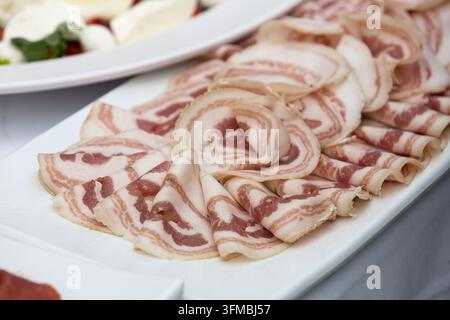 Sliced pancetta for appetizers on a white plate ready for a catering event Stock Photo