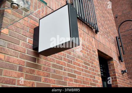 Blank rectangular storefront signboard mounted on red brick facade beneath black metal window grille at outdoor entrance on street angled low Stock Photo