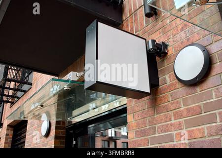Blank rectangular storefront signboard mounted on red brick facade beneath black metal window grille at outdoor entrance on street angled low Stock Photo