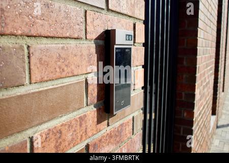 Smart doorbell camera mounted on red brick exterior wall beside residential front door in daytime, showing illuminated ring button, lens, and security Stock Photo