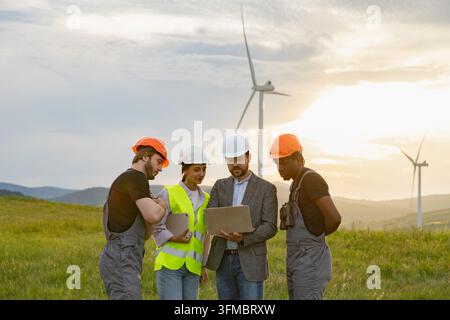 Diverse team of engineers collaborating on a wind farm project at sunset Stock Photo