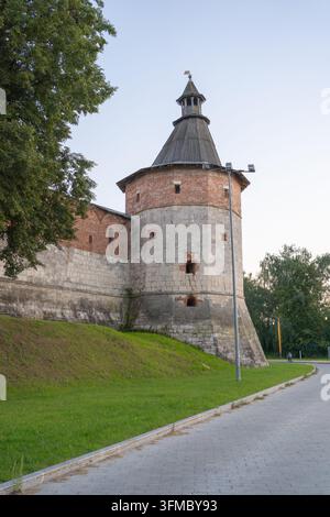 a tranquil historical tower remains motionless on a grassy hill beside a paved path, bathed in natural daylight, showcasing brick, stone, and wood Stock Photo