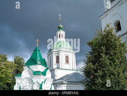 Church standing, in outdoor cloudy sky, with church, green domes, crosses, trees, from a low angle looking up perspective, with white, green accents Stock Photo