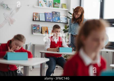 Schoolchildren using tablets and artificial intelligence tools for learning in classroom. Stock Photo