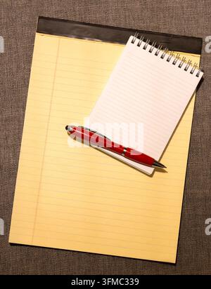Top view of blank yellow lined legal paper pad with small spiral notebook and a red ballpoint pen on grey fabric background Stock Photo