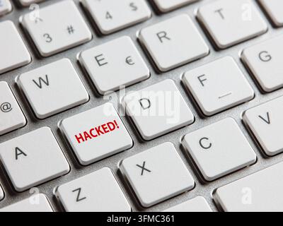 Computer keyboard showing a red HACKED key, symbolizing data breach, cyber attack, and internet vulnerability Stock Photo