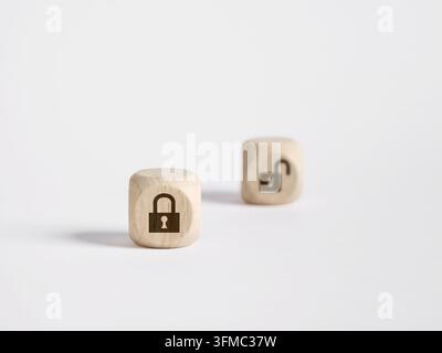 Two wooden cubes representing security concepts with a locked padlock symbol in focus and an unlocked padlock in background Stock Photo