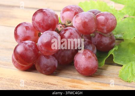 Fresh Red Globe Grapes Bunch with Leaves on Wooden Table Surface Stock Photo