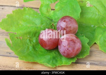 Fresh Red Globe Grapes Bunch with Leaves on Wooden Table Surface Stock Photo
