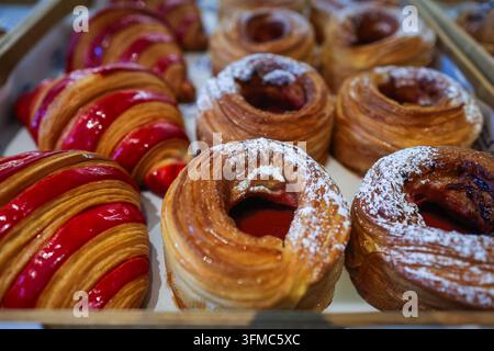 Golden, flaky layers and a glossy red glaze: fresh-baked croissants and jam-filled laminated pastry rings, fresh from the bakery tray. Stock Photo