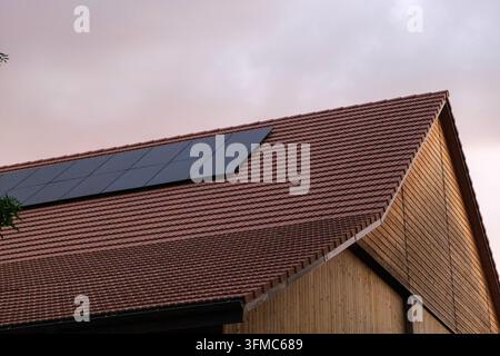 Solar panels are installed on a barn roof, showcasing a renewable energy solution in a rural setting during the evening. Stock Photo