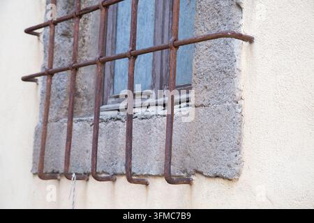 Rusty iron window bars on old stone wall with weathered plaster, cracked masonry, faded blue window frame, and aged architectural texture showing Stock Photo