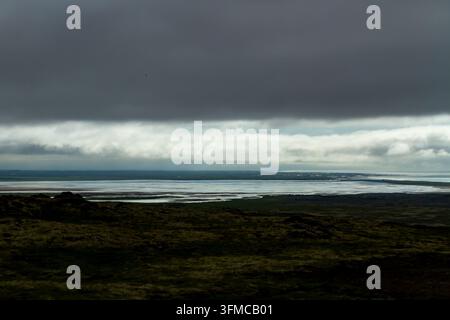 Dark storm clouds over a quiet coastal wetland, with pale light breaking across the distant sea and tidal flats. Stock Photo