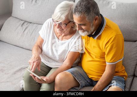 Senior couple using smartphone together while sitting on sofa at home Stock Photo