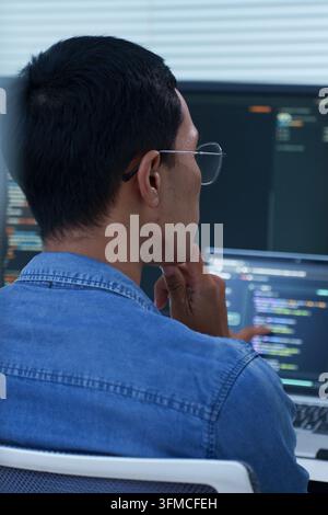 A focused developer wearing glasses studies computer code while working on software development and digital technology projects. Stock Photo