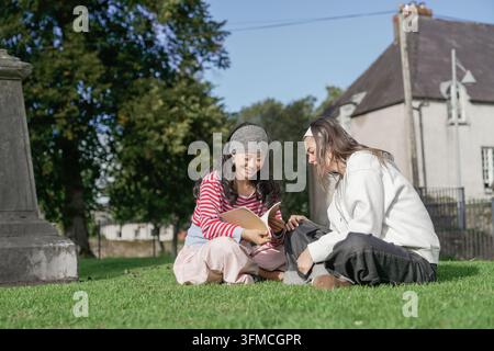 Young women studying together outdoors on green grass Stock Photo