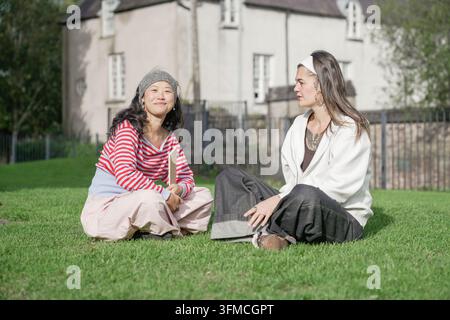 Diverse women friends sitting on grass conversing outdoors Stock Photo
