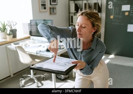 Middle Aged Businesswoman Dancing while Analyzing Financial Report in Office Stock Photo