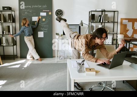 Adult Man Dancing While Typing on Laptop in Creative Office Stock Photo