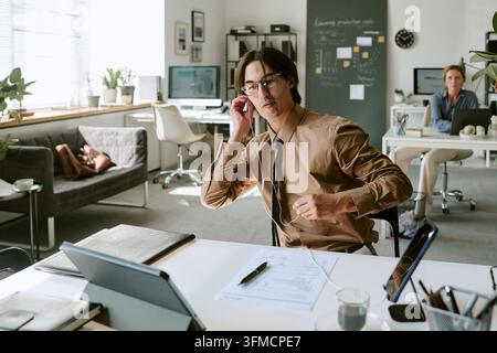 Adult Man Wearing Earphones Sitting at Desk in Office Stock Photo