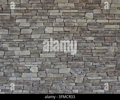 Flat stone wall with varied rectangular rocks showing natural tan, white, light gray and variegated coloration, uneven geological textures Stock Photo