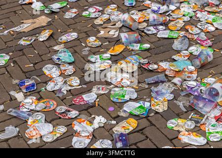 Zwolle, Netherlands - 23 August 2026 - Crushed aluminum soda cans, plastic cups and litter scattered on cobblestone street after festival event. Stock Photo