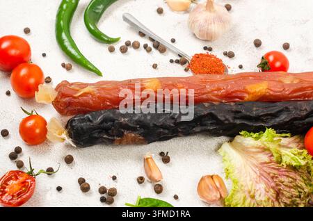 assorted smoked and cured sausages arranged with fresh chili peppers, garlic, cherry tomatoes, lettuce, basil, bay leaves, paprika, and black pepper. Stock Photo