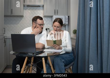 Couple sitting at a table in their kitchen, analyzing personal financial documents and using a laptop, representing remote work, budgeting, and shared Stock Photo