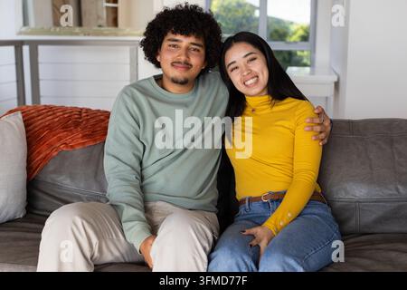African American couple sitting, smiling on gray leather sofa in home with orange throw Stock Photo
