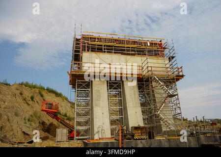 Concrete bridge pier under construction surrounded by steel scaffolding on an industrial job site under a cloudy sky, heavy civil engineering, industrial building site Stock Photo