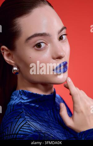 Fashionable woman showcases bold blue lipstick and velvet bodysuit in artistic pose Stock Photo