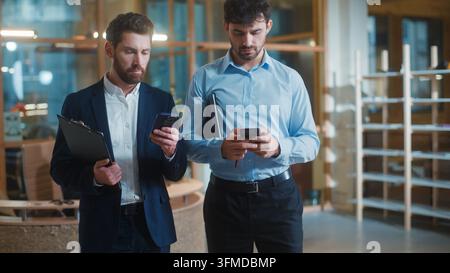 Two gadget addicted Caucasian business men using mobile phones scrolling social media in office. Concentrated businessmen male colleagues workers Stock Photo